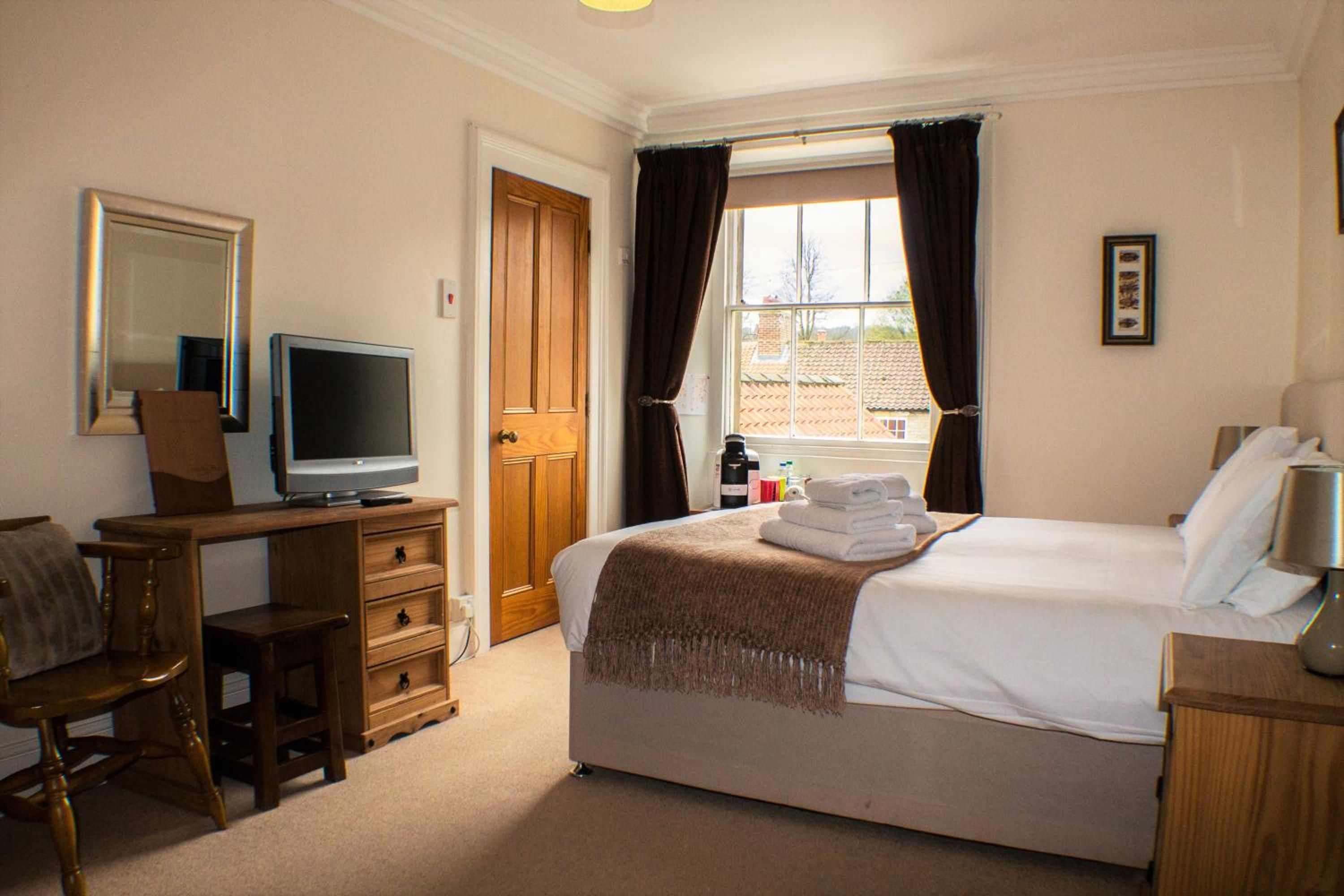 A hotel room with a bed, a TV, a desk, a chair, a wardrobe, and a window with curtains.