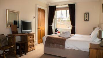 A hotel room with a bed, a TV, a desk, a chair, a wardrobe, and a window with curtains.