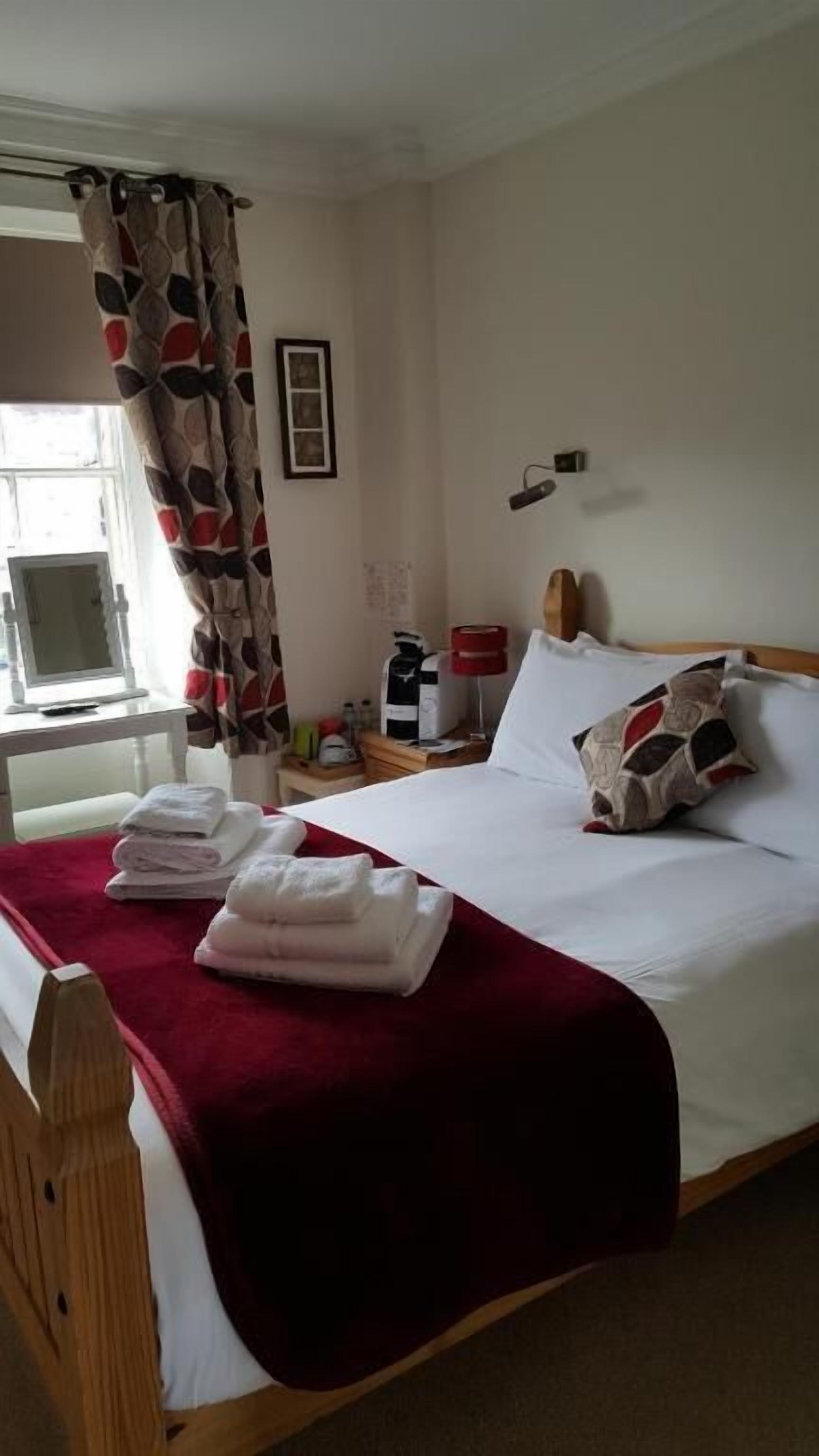 A hotel room with a bed, a bedside table, a lamp, and a window with curtains.