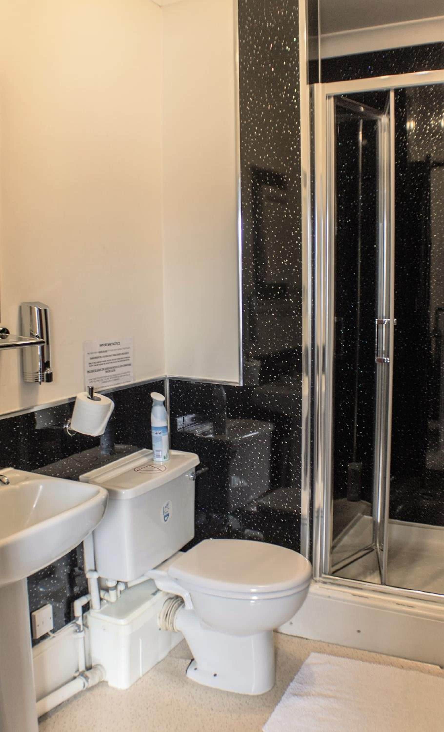 A bathroom with a toilet, bidet, and sink. There is a glass shower door and a sign on the wall.