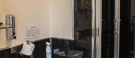 A bathroom with a toilet, bidet, and sink. There is a glass shower door and a sign on the wall.
