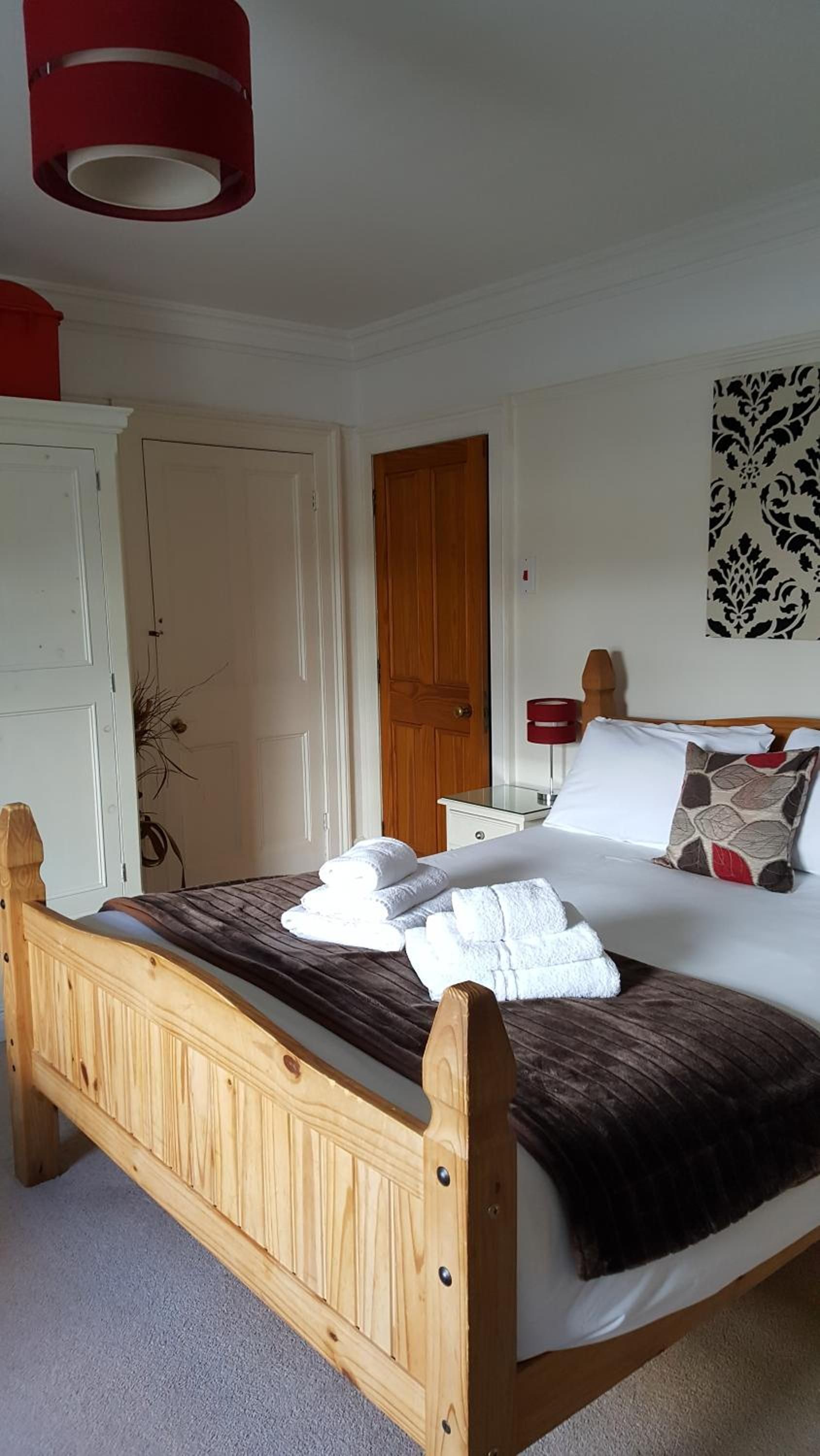 Quarto com cama de madeira, paredes brancas, porta de madeira e abajur vermelho.