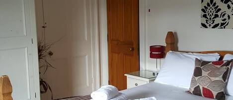 Quarto com cama de madeira, paredes brancas, porta de madeira e abajur vermelho.