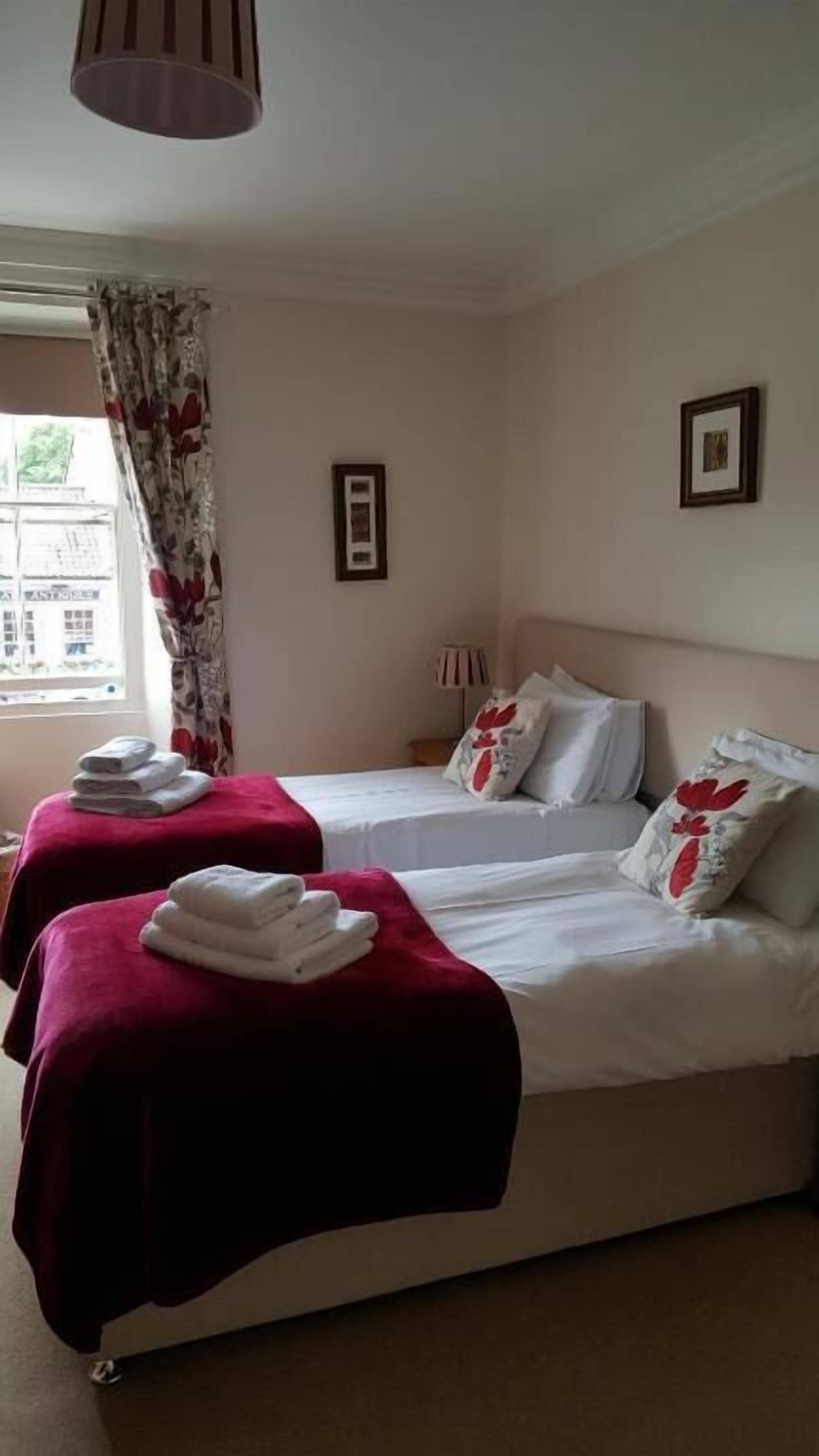A hotel room with two beds, a window with curtains, and a lamp on the nightstand.