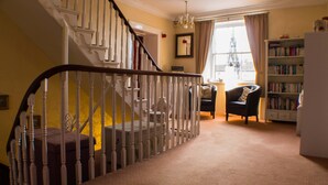 A staircase with white balusters, a chandelier, a bookshelf, and a window with a view of a tower. - The Royal Oak Hotel (York)