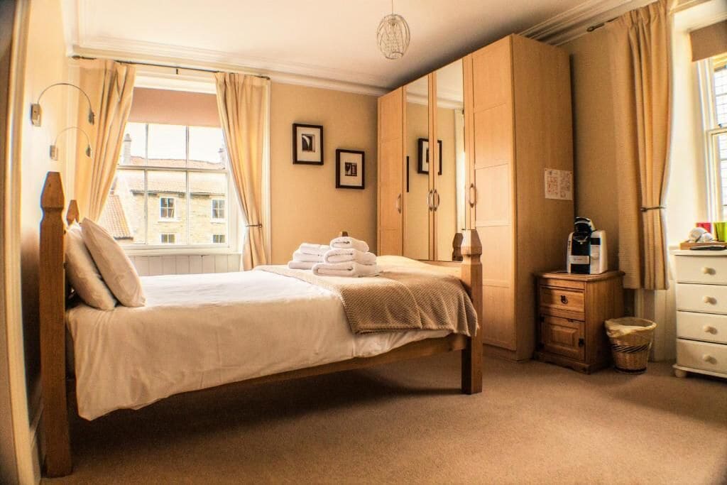 Un dormitorio con cama, armario, mesita de noche y ventana con cortinas.