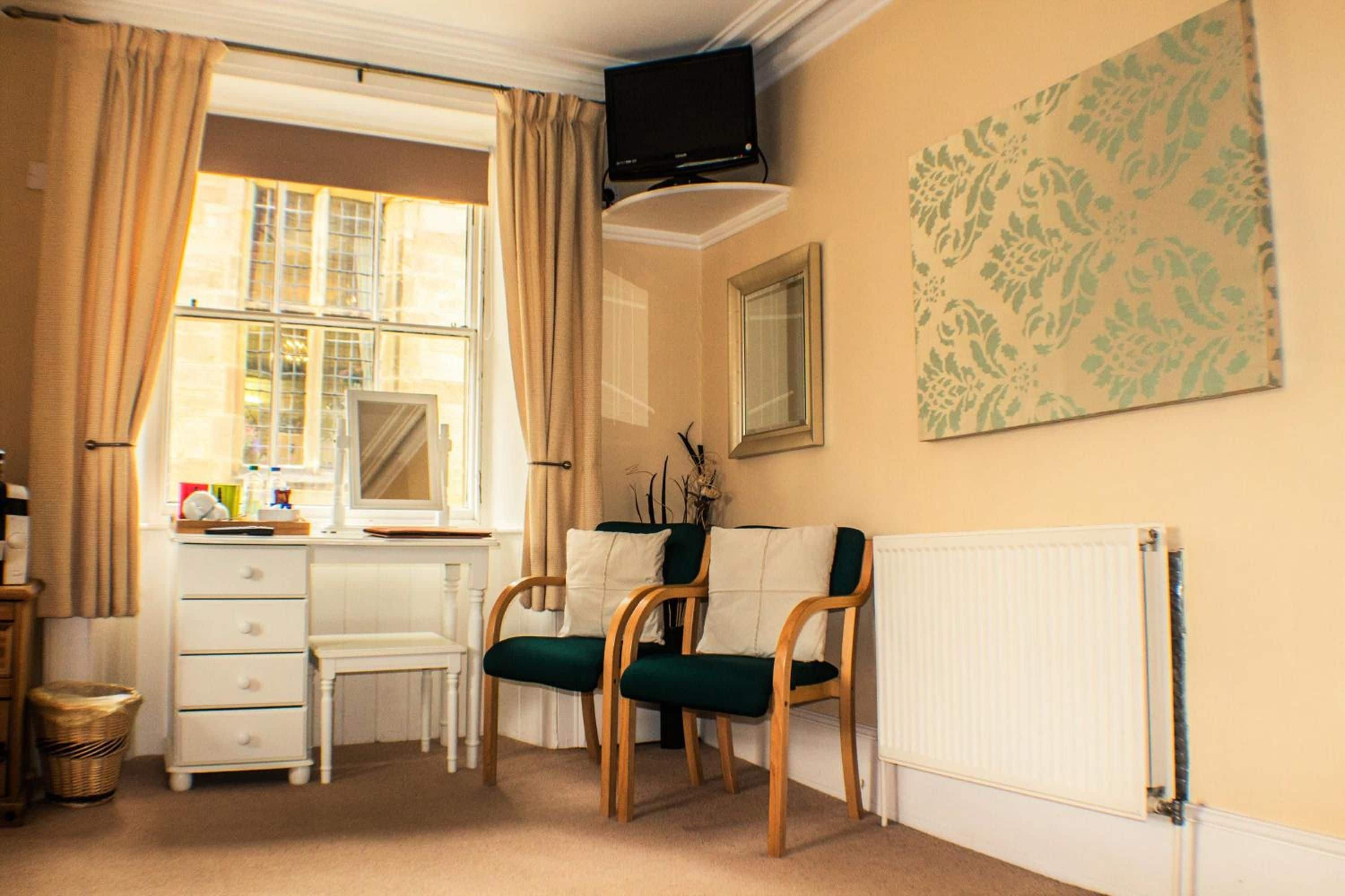A room with a desk, two chairs, a radiator, and a window with curtains.