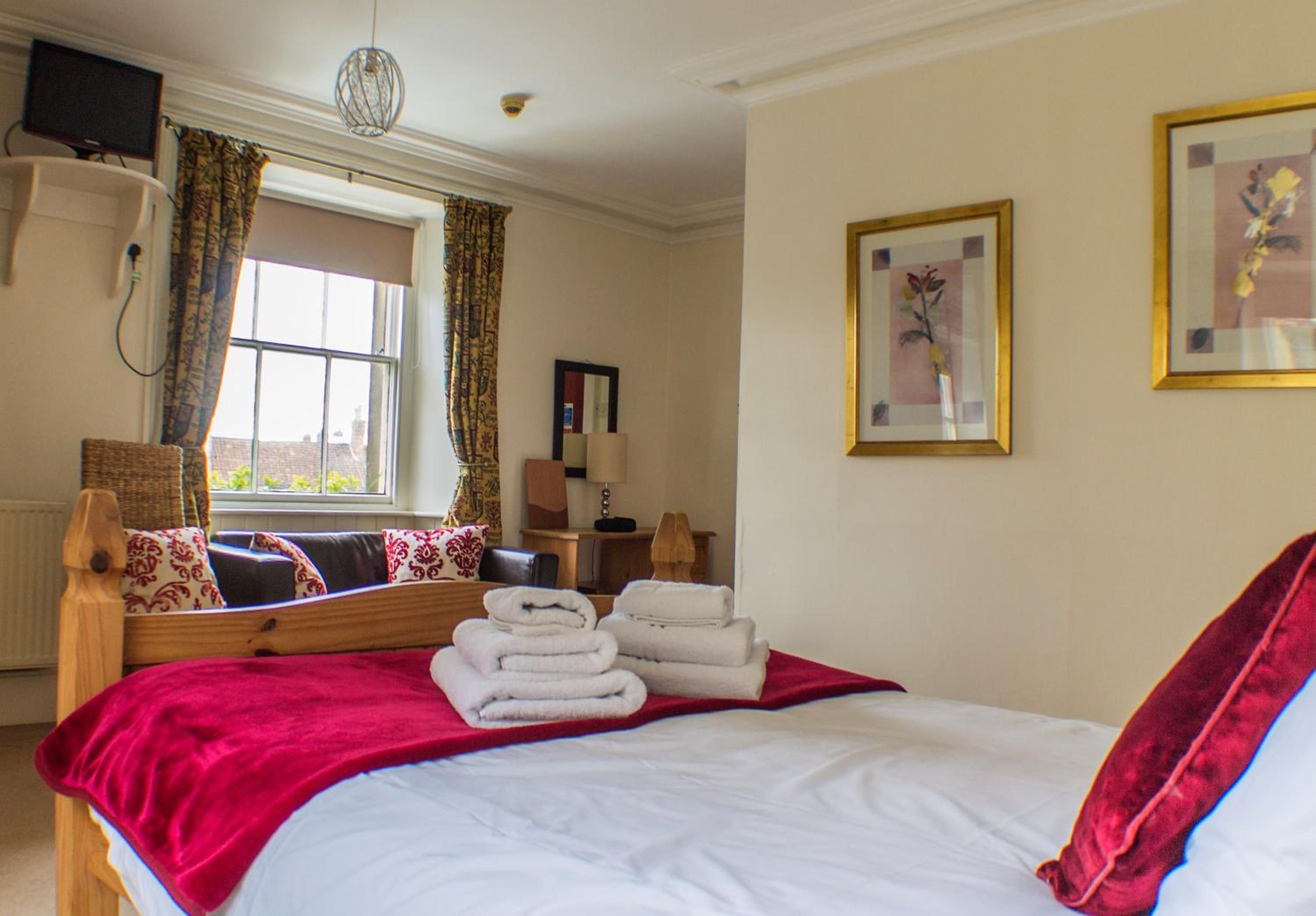 A hotel room with a bed, a window, a flat-screen TV, a lamp, and a framed picture on the wall.