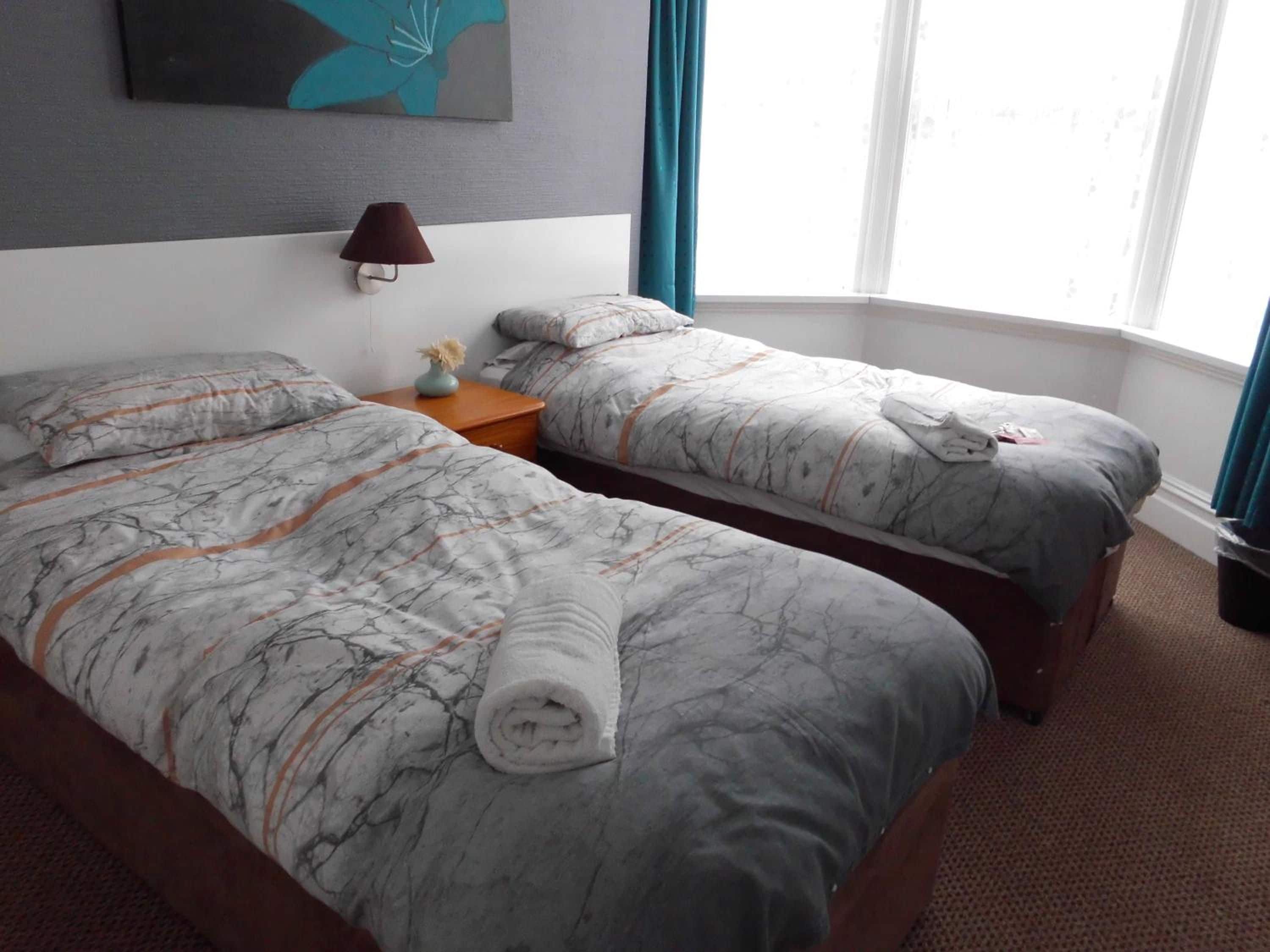 Habitación de hotel con dos camas, una mesita de noche, una lámpara y una ventana con cortinas.