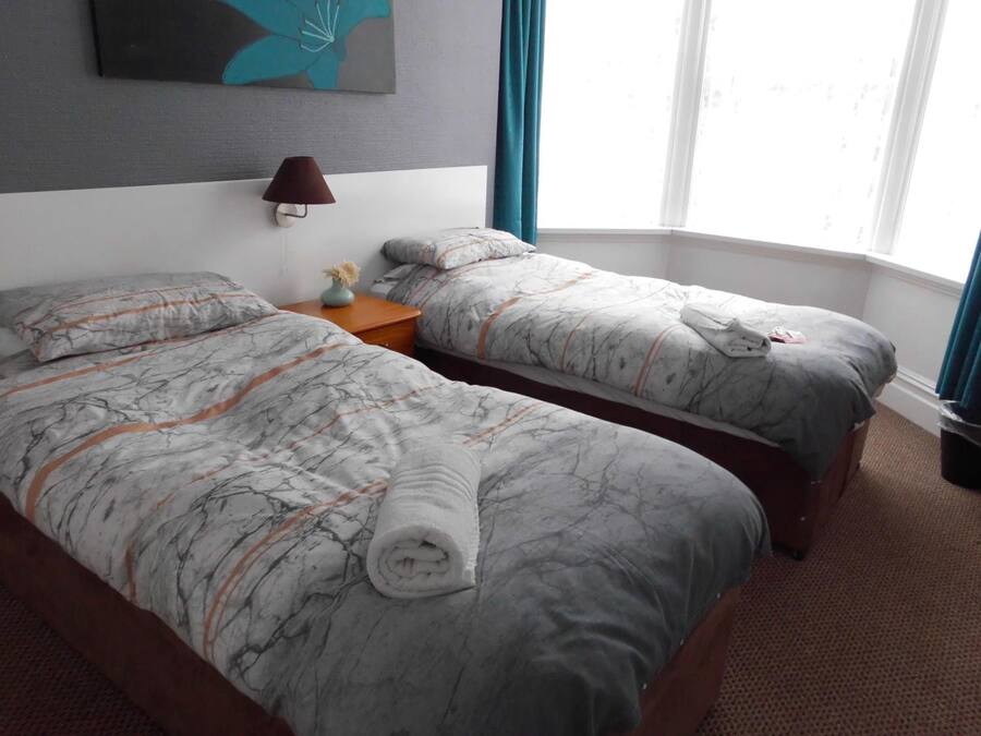 A hotel room with two beds, a nightstand, a lamp, and a window with curtains.