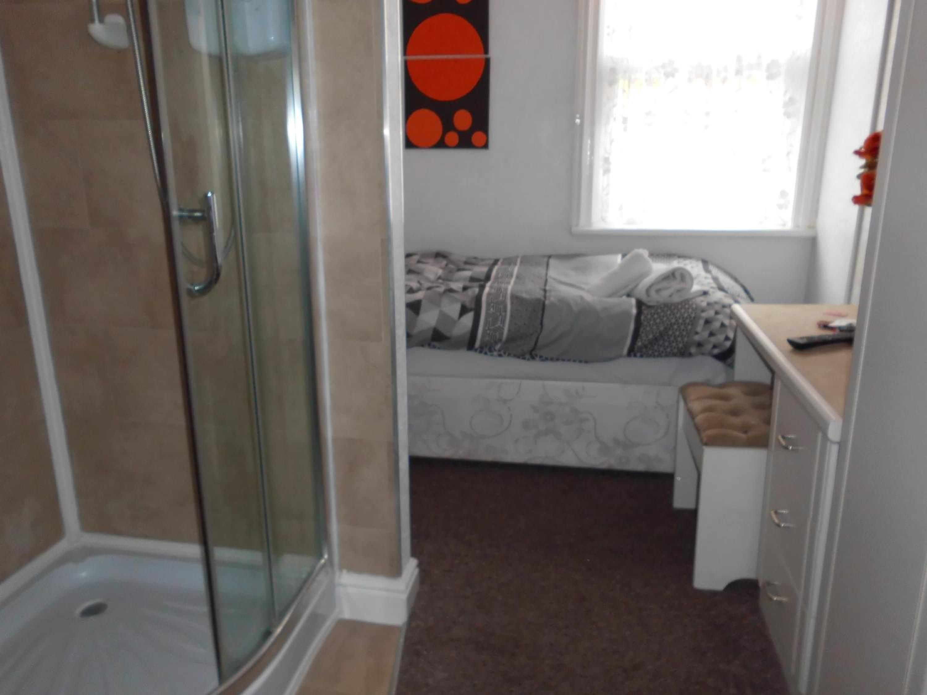 A bathroom with a glass shower enclosure, a bed with a patterned bedspread, and a window with a view.