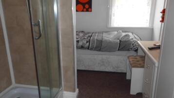 A bathroom with a glass shower enclosure, a bed with a patterned bedspread, and a window with a view.
