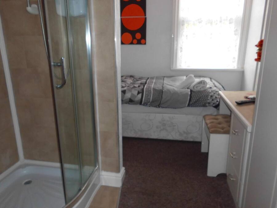 A bathroom with a glass shower enclosure, a bed with a patterned bedspread, and a window with a view.