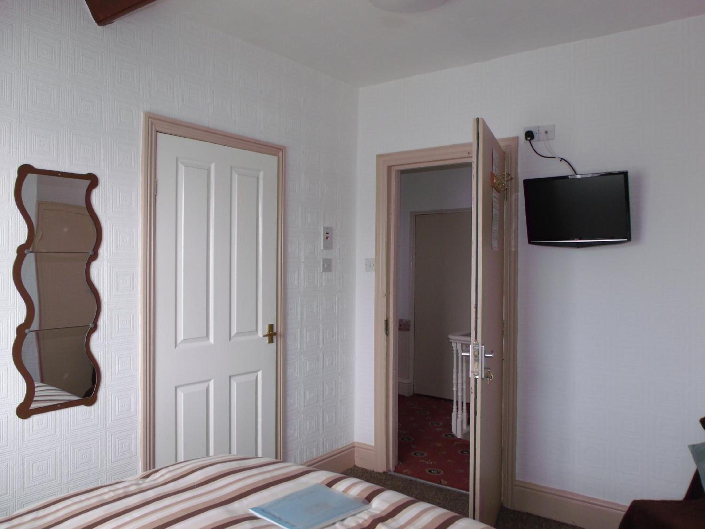 A hotel room with a bed, a television mounted on the wall, and a door leading to another room.