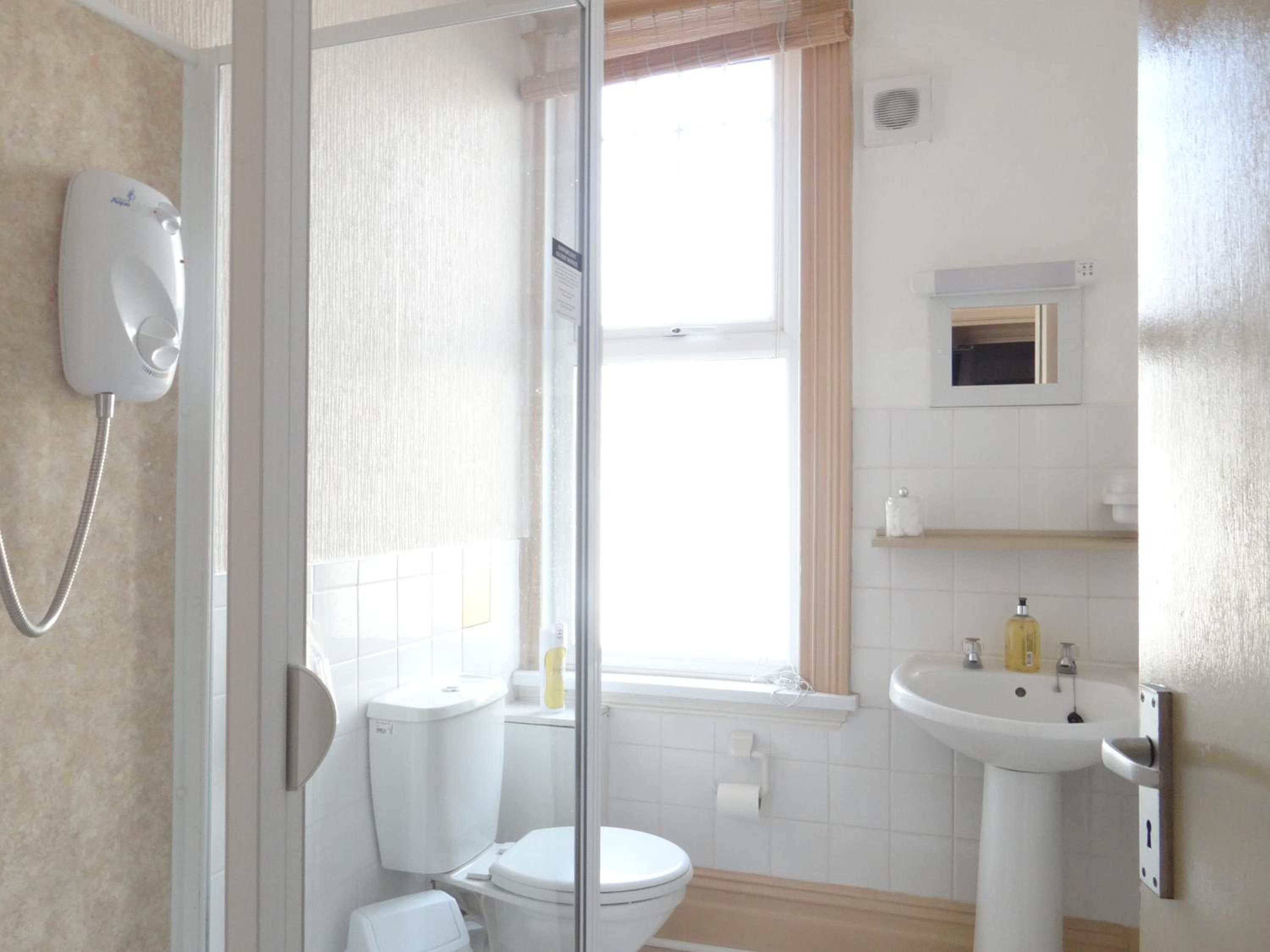A bathroom with a toilet, a glass-enclosed shower, a sink, and a window with curtains.