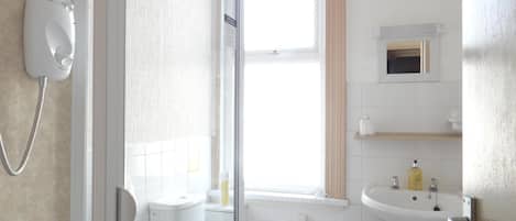 A bathroom with a toilet, a glass-enclosed shower, a sink, and a window with curtains.