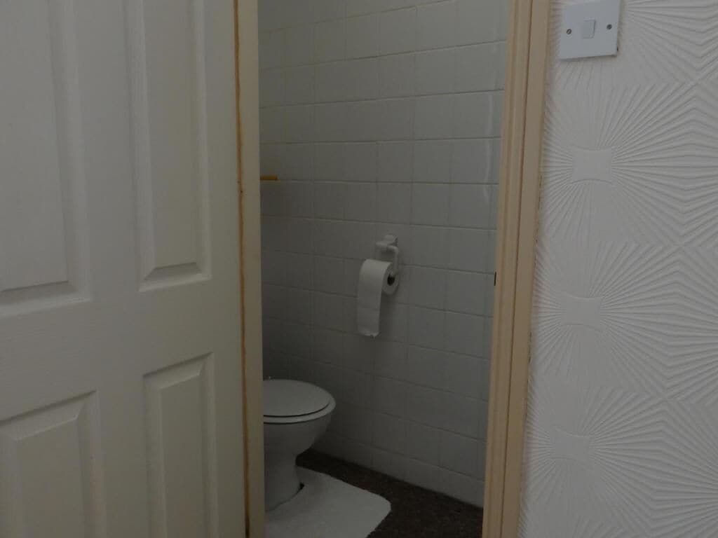 Kylpyhuone, jossa on wc, wc-paperirulla ja valkoinen ovi.