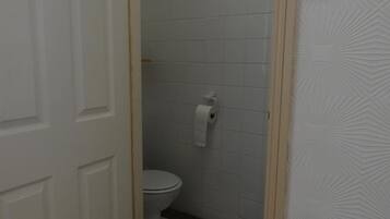 Un baño con un inodoro, un rollo de papel higiénico y una puerta blanca.
