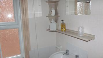 A bathroom with a window, a sink, a mirror, and shelves with toiletries.