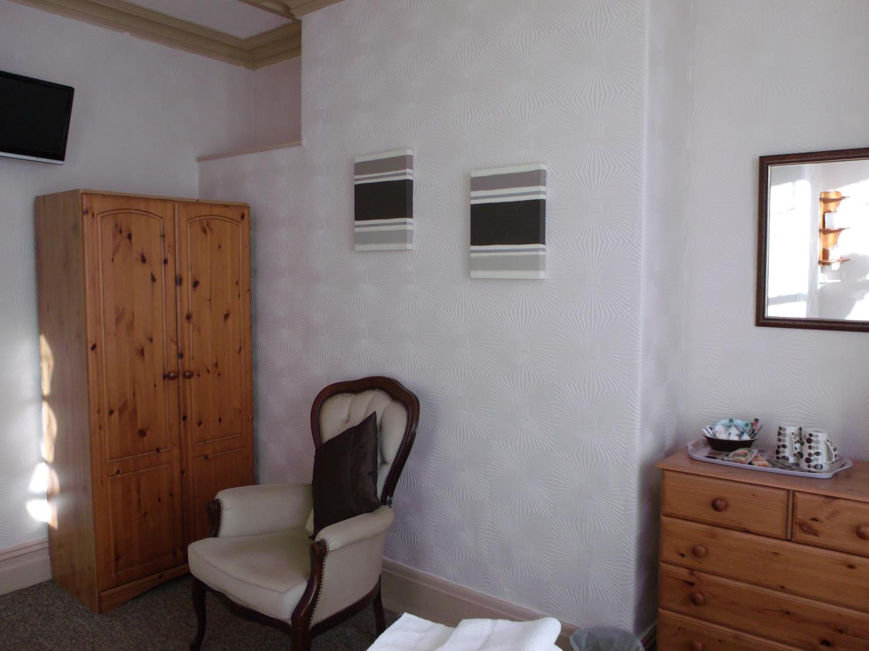 Un dormitorio con un armario de madera, una silla, un tocador y un espejo en la pared.