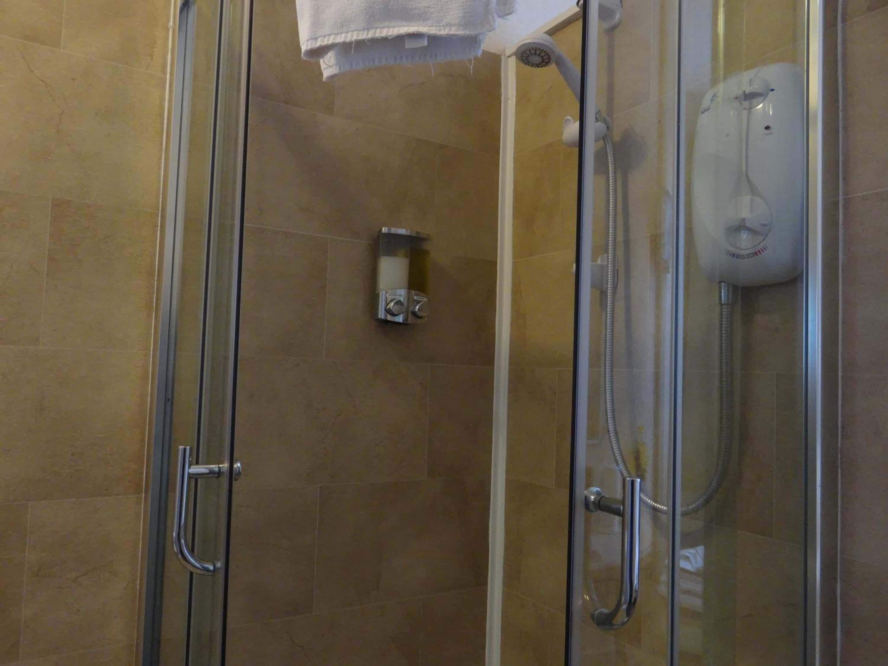 A glass-enclosed shower stall with a handheld showerhead and a wall-mounted control panel.