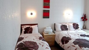Una habitación de hotel con dos camas, una mesita de noche con lámpara, y un aplique en la pared.
