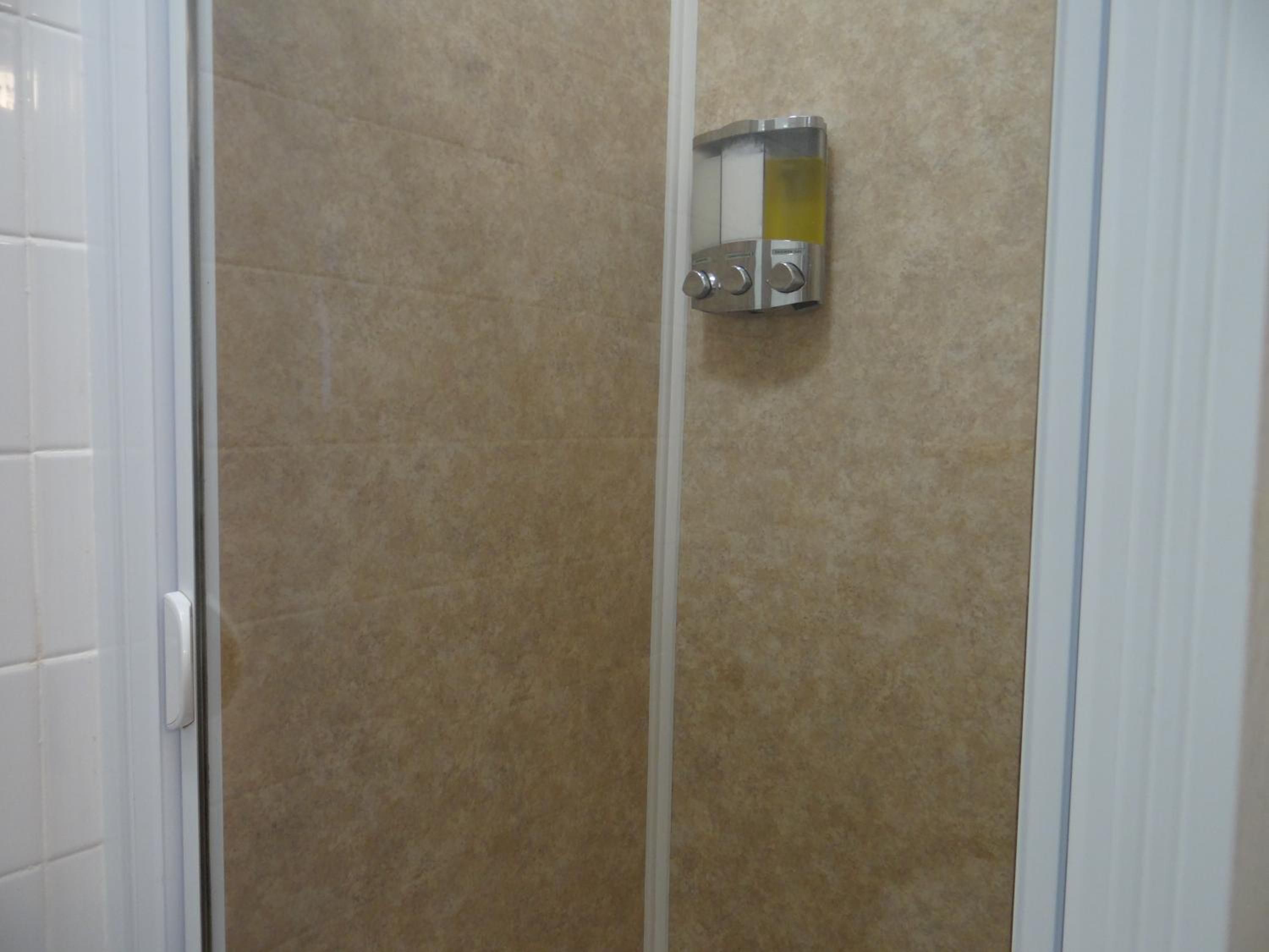 A bathroom with a shower enclosure, a white door, and a wall-mounted control panel.
