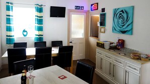 Un comedor con una mesa, sillas, un televisor y una encimera de cocina con diversos objetos.