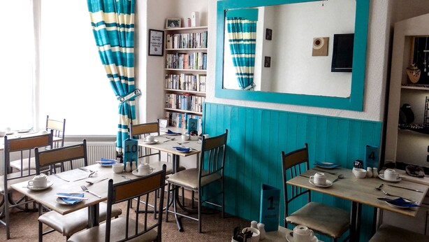 Un comedor con mesas y sillas, una estantería y un espejo.