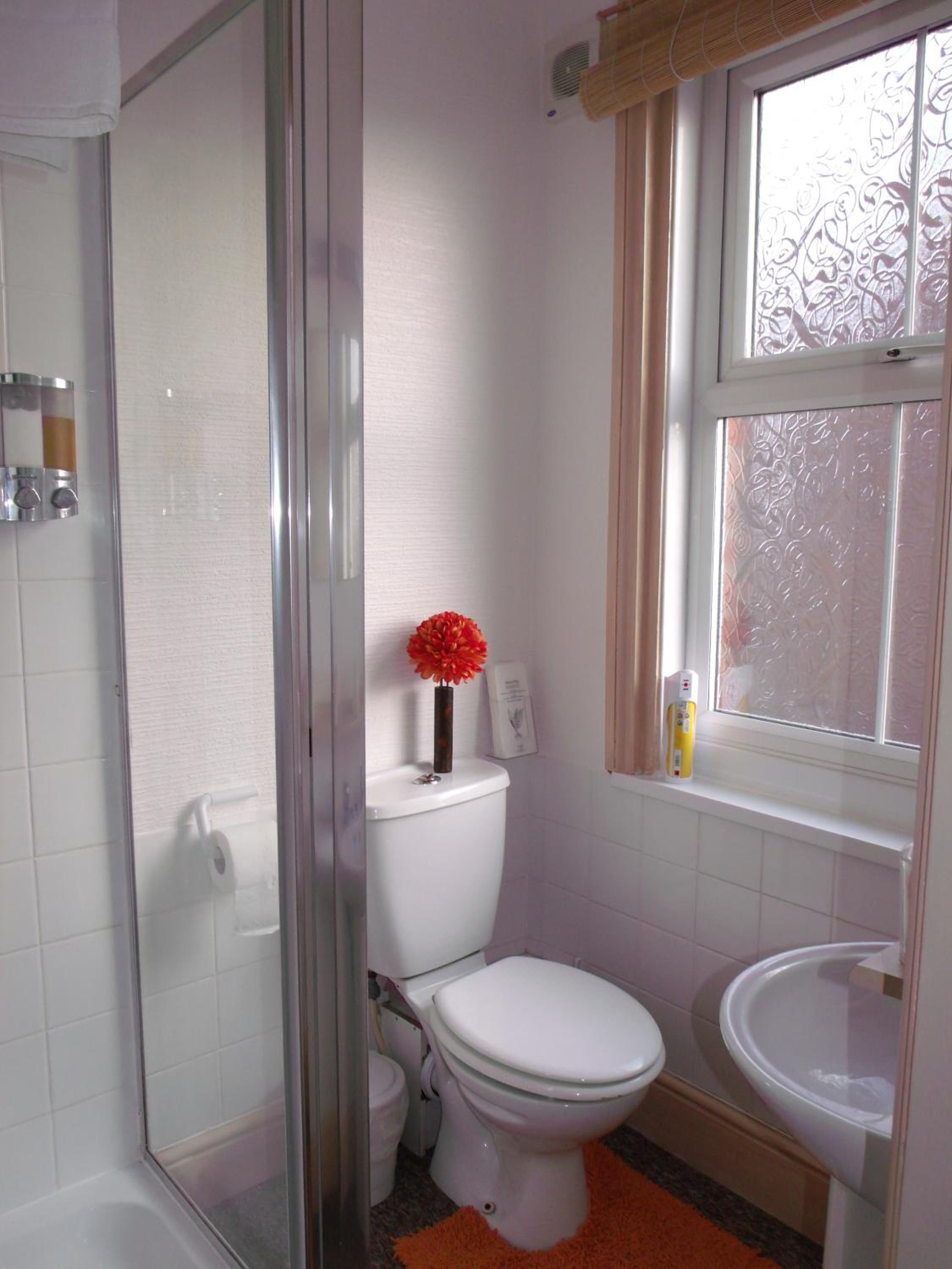 Une salle de bain avec une douche à parois de verre, des toilettes, un lavabo et une fenêtre ornée de vitraux.