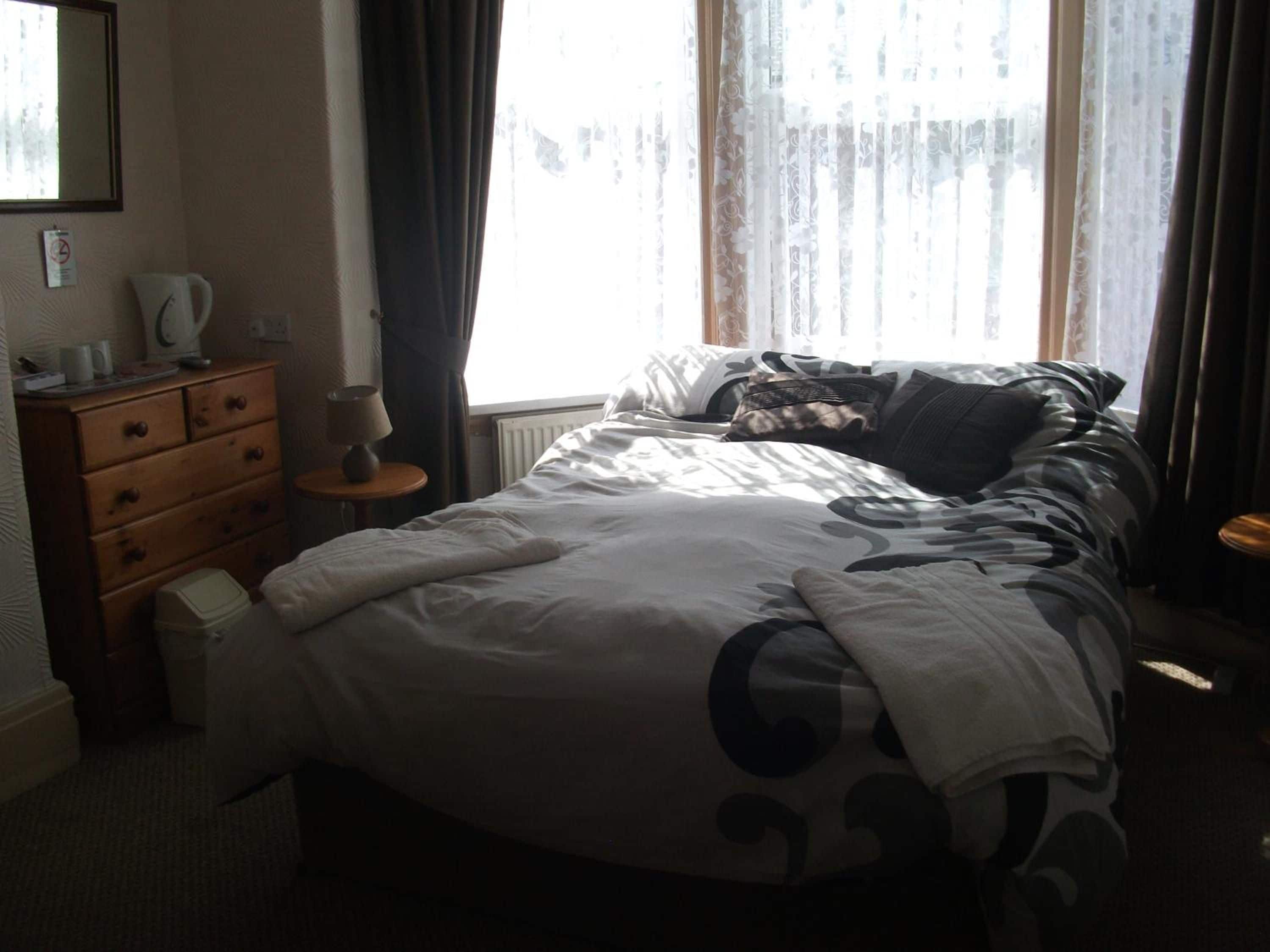 A hotel room with a bed, a dresser, a lamp, and a window with curtains.