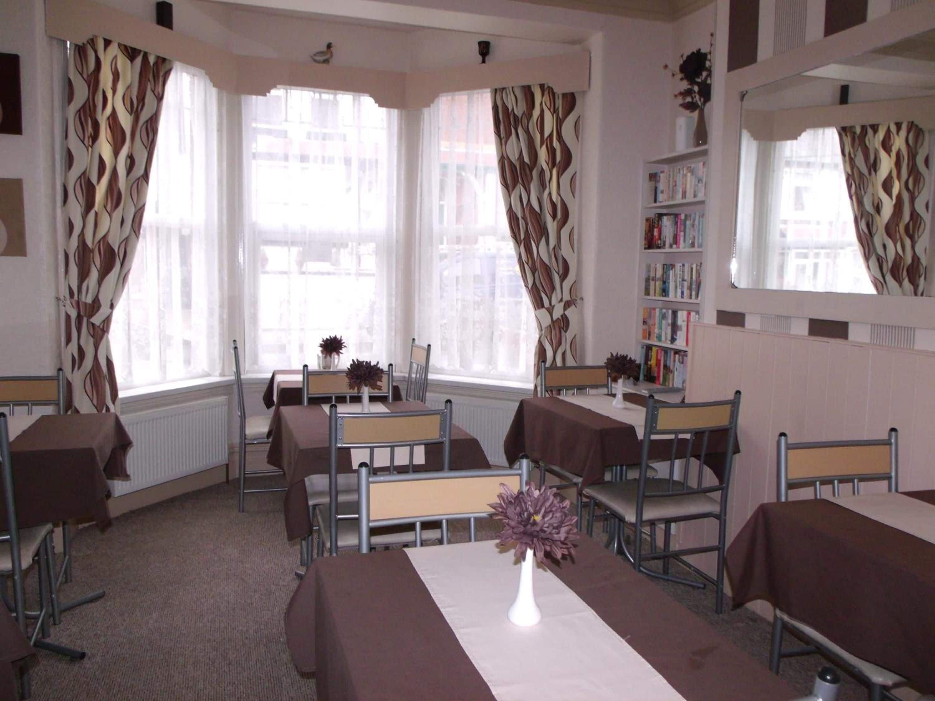 A hotel room with a dining area, a bookshelf, and large windows with patterned curtains.