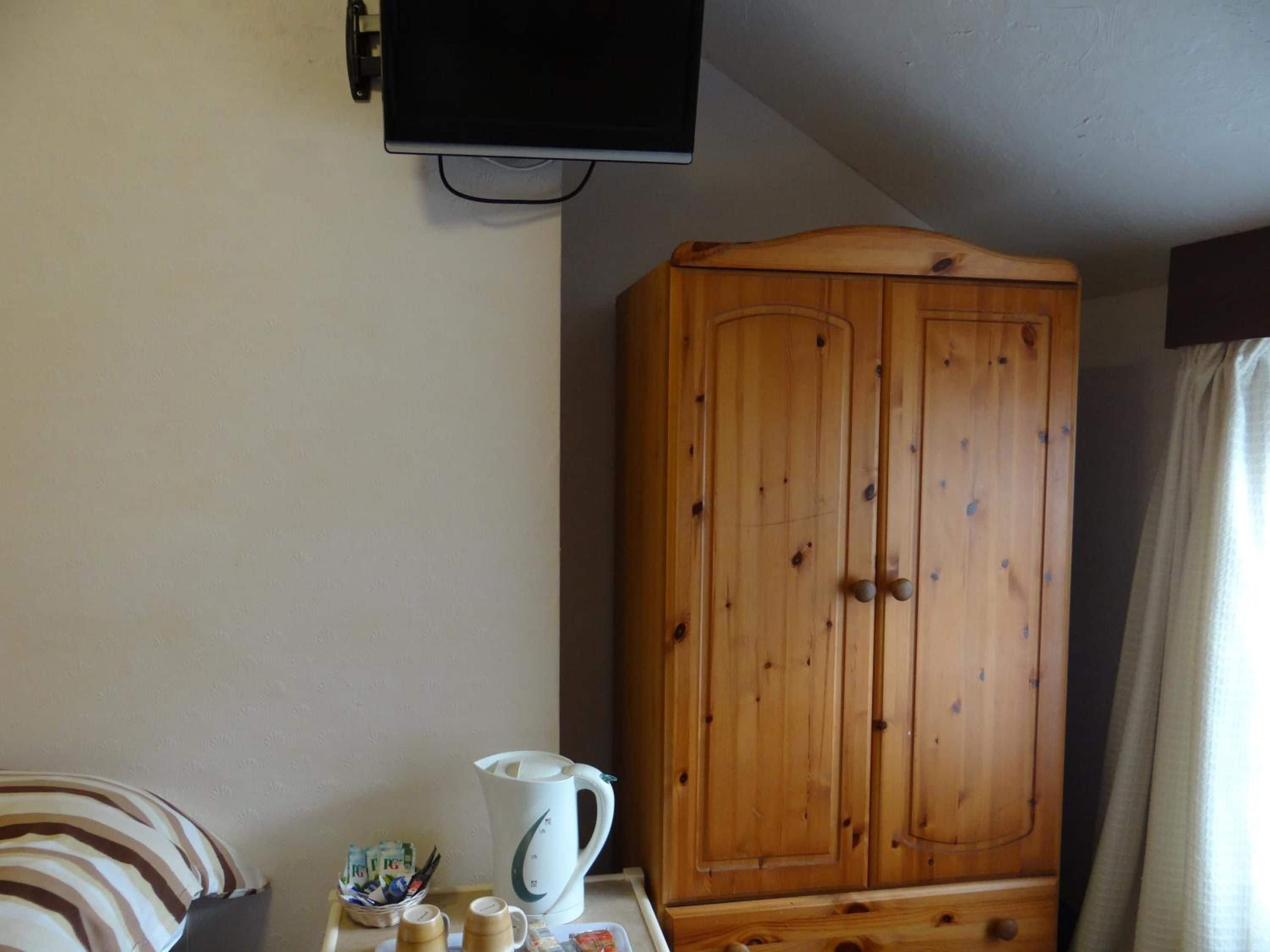 A room with a wooden wardrobe, a television mounted on the wall, and a table with a kettle and cups.