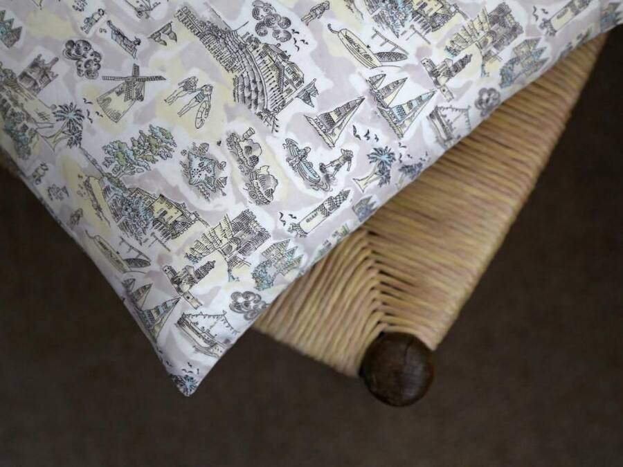 A bed with a patterned bedspread featuring various architectural and cultural illustrations.