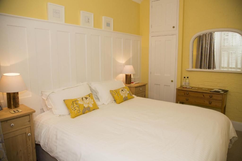 Une chambre à coucher comprenant un lit, deux tables de chevet, une commode, une coiffeuse, une fenêtre avec des rideaux et une porte.