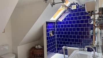 A bathroom with a skylight, a bathtub, and a shower area with blue tiles.