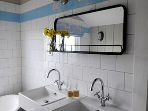 A bathroom with two sinks, a mirror, and a shelf with flowers.