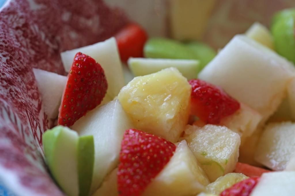 En skål med frugtsalat med jordbær, æbler og pærer.