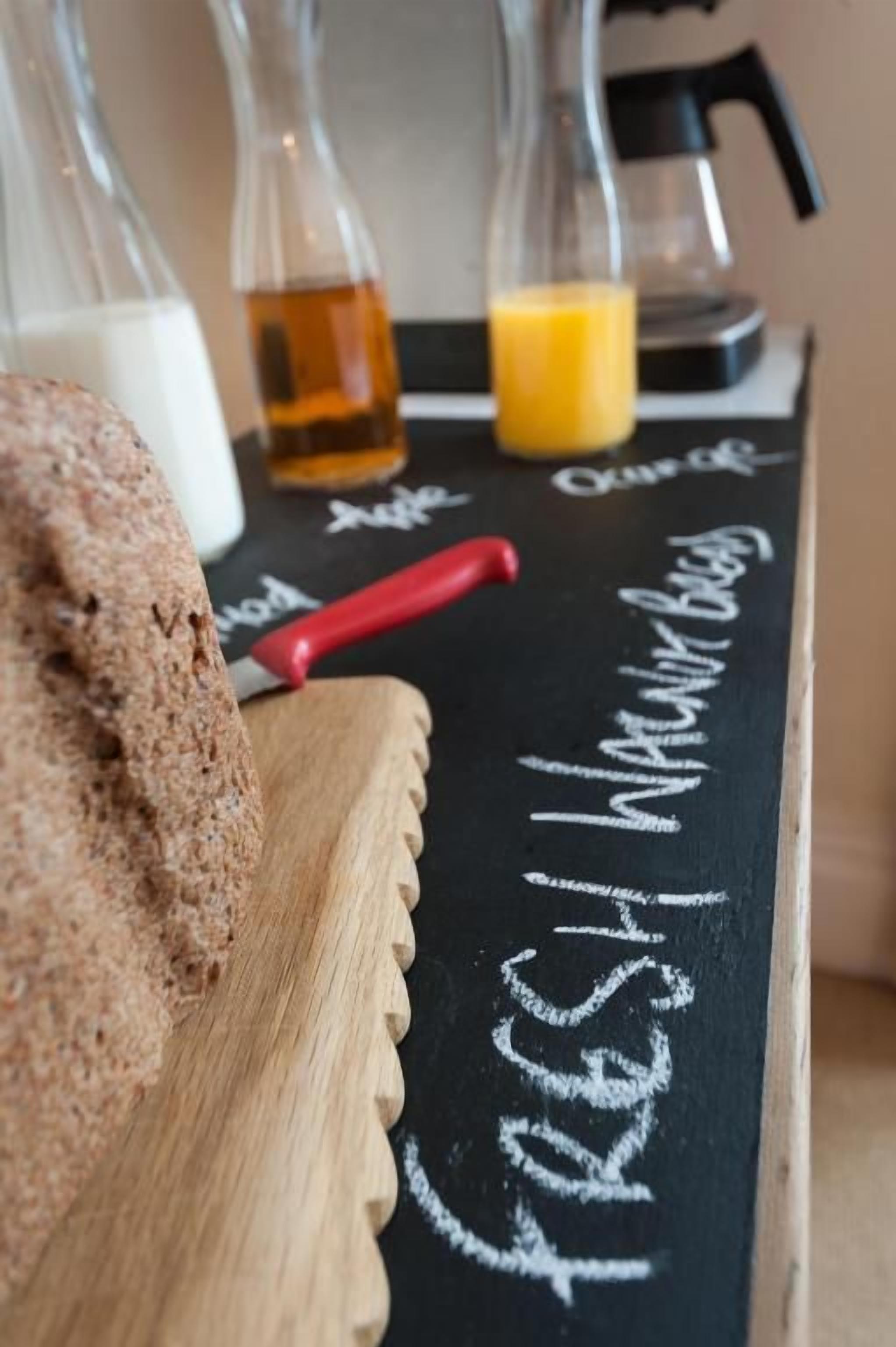 A chalkboard with the words 'fresh' and 'warm' written on it, a red-handled knife, and a loaf of bread.
