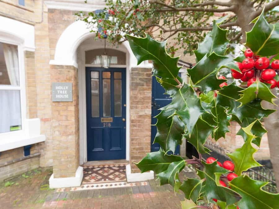 A traditional brick building with a blue door and a sign reading "HOLLY TREE HOUSE".