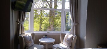 A room with a large window, two armchairs, a small table, and a TV mounted on the wall.