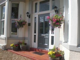 A building with a front door, two hanging flower baskets, and two potted plants on the steps.