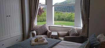 A bedroom with a bed, a small table, and a window with a view of a green landscape.