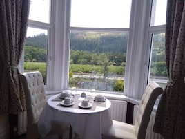 A dining area with a table set for four, overlooking a scenic landscape with a river and forest.
