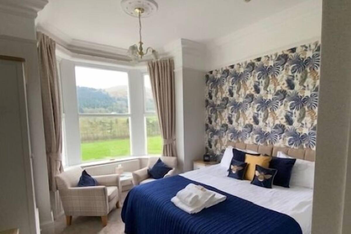 Une chambre avec un grand lit, une vue sur l’extérieur, une fenêtre avec des rideaux et un mur décoré de motifs.