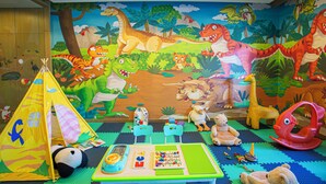 Un cuarto de juegos infantil con un mural de dinosaurios, una carpa de juegos y diversos juguetes.