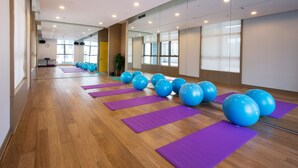 Amplia habitación con suelo de madera, colchonetas de yoga moradas y pelotas de ejercicio azules dispuestas en fila.