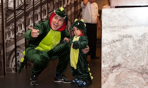 Una persona vestida de dinosaurio verde posa con un niño que lleva un disfraz parecido.