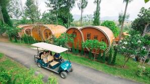 A golf cart on a paved road with a row of cylindrical treehouses in the background. - Raisongrao Resort (Khao Kho)
