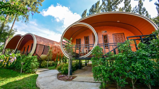 A series of cylindrical, red-roofed cabins with a balcony, surrounded by lush greenery and trees. - Raisongrao Resort (Khao Kho)